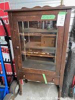 Front view of vintage wooden china cabinet with glass door, door knob, and drawer below.