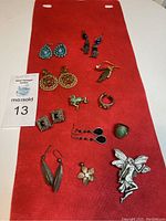 Photo showing assortment of earrings, rings, brooches, and pendants arranged on red background cloth, including the flower pendant and pewter brooch.