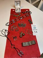 All vintage jewelry items displayed on a red cloth including earrings in box, bracelets, Murano glass necklace, and multiple earring sets.
