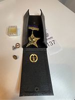 Photo showing all items: vintage medal in black case with four pins arranged nearby including Sterling marked pin.