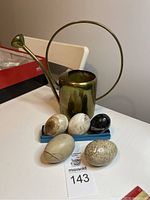 Full lot showing the brass watering can with five oval stones arranged in front on a small tray.