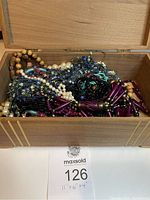 Open wooden jewelry box revealing assorted jewelry including bead and pearl necklaces and two bracelets