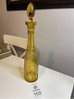 Full view of the tall yellow glass decanter with stopper showing overall shape and decorative etching.