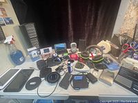 Wide view of the lot showing headphones, chargers, tablets, digital scales, and various cables on a table.