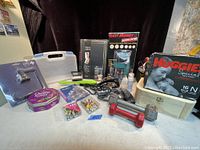 General view of the 16 miscellaneous items in the lot including tools, photo albums, candy tin, baby wipes tin, and assorted smaller items.