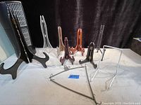 Nine assorted plate and platter holders in various sizes and colors arranged on a beige surface.