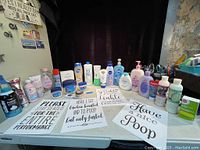 Overview of products including hand creams, shampoos, body washes, and decorative bathroom signs laid out on a table.