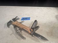 Multi-tool displayed open showing hammer head, screwdrivers, knife blade, and pliers with wood handle.