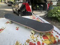 Side view of the skateboard showing grip tape and some wear.