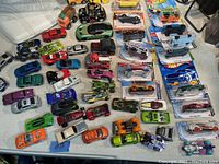 Large assortment of approximately 50 toy cars including loose and packaged items from Hot Wheels, Mattel, Matchbox, and Maisto, showing variety of colors and condition.