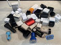 Top down view showing a large assortment of USB wall and car plug chargers mostly in black and white plastic with some color variations and extras.