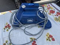 Blue Dirt Raider hand vacuum with long gray cord wrapped around it, placed on a floral patterned cloth.