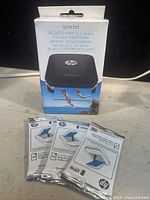 Boxed HP Sprocket portable photo printer with three sealed packs of print paper in front.