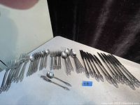 Full view of the spread-out cutlery set showing spoons, forks, knives, and spreader with detailed floral patterned handles.