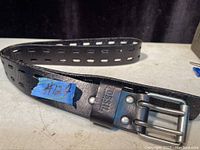 Photo of Fossil black leather belt with metal buckle showing Fossil brand imprint on leather near buckle and rectangular punched holes.