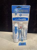 Front view of sealed Vital Health powered oral care system with toothbrush, brush heads and accessories visible