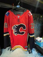 Front view of the red Calgary Flames NHL hockey jersey featuring number 28 on the sleeves and front, hanging on a hanger.