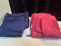 Photo showing folded dark blue queen size comforter and matching pillow shams on the left, and folded solid red queen size sheet set (top sheet, fitted sheet, two pillowcases) on the right.