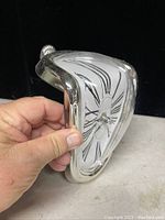 Photo showing the side view of the novelty melting style clock held by a hand to show shape and scale.