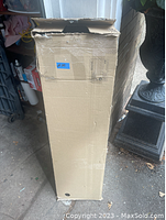 Tall rectangular cardboard box containing packaged bookcase parts, sealed but with some wear and dents.