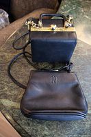 Two black purses, one square box style with gold hardware, and one with Anne Klein II logo embossed on front.