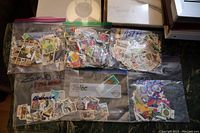 Six clear ziplock bags filled with loose used postage stamps from various countries and regions, laid out on a surface.