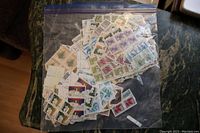 Photo of assorted used Canadian stamps and plate blocks inside a clear resealable plastic bag placed on a dark surface, showcasing various designs and colors.