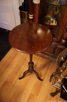 Full view of mahogany plant stand showing round top and tripod base, wood grain visible.