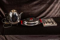 Overview photo showing all three items: vintage chrome coffee percolator with black base and handles, MCM serving dish with lid and red handles, and Swissmar cheese cutter set in original packaging.