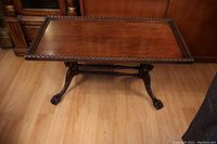 Front view of solid walnut coffee table with carved border and claw feet on hardwood floor.