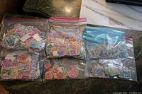 Six bags of older used United States postage stamps displayed on a surface, showing a variety of colors and stamp designs.