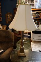 Front view of one brass lamp with silk shade on table near brown chair showing overall shape and condition.