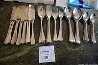 Complete set of 18 pieces of WMF Chromargan stainless steel cutlery arranged in order: knives, forks, large spoons, small spoons on a stone surface with a note card showing lot details.