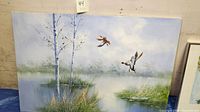 Oil on canvas painting showing a marsh landscape with two geese in flight and thin trees on the left side, details of grass, water reflections and misty background
