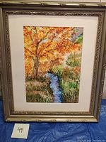 Framed watercolor painting showing flowing stream and autumn landscape with orange and yellow foliage.