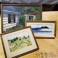 Three framed watercolor paintings: a garden scene, a coastal seascape, and a landscape with cottages, all signed.