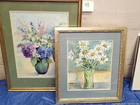 Two framed watercolor paintings showing floral bouquets. One has white daisies, the other features purple and pink flowers including hydrangeas.