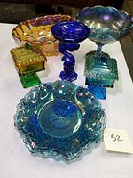 Photo of five colored depression glass items: blue iridescent bowl, cobalt blue fish shaped candle holder, turquoise compote dish, yellow lidded candy dish with green base, and yellow bowl.