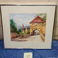 Full front view of the framed watercolor painting showing the architecture courtyard scene with an archway, distant mountains, and buildings with red-tiled roofs and church-like spires.