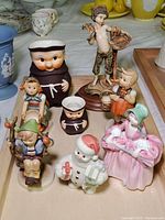 Overview of Goebel friar pitcher figurines, Hummel figurines, Lenox Santa, and Royal Doulton figurine on wooden tray (not included)