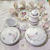 Overview of the Royal Albert Braemar demitasse set with cups, saucers, serving bowls, sugar pot, sauce boat, and Meakin teapot arranged on white cloth.