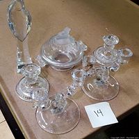 Lot showing all four glassware items on a table: signed glass figurine, candy dish with lid, and two three-arm glass candleholders.