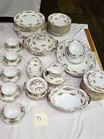 Full view of Noritake china dinnerware including stacked plates, teacups with saucers, serving bowls with lids, and serving platters all decorated with floral and gold accents.