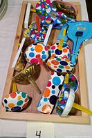 Lot of tin New Year's Eve party noise makers with wooden handles arranged in wooden tray.