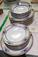 Stacked sets of dinner plates and bowls featuring blue floral and gold lined rim design on white porcelain.