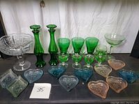 Full lot showing green glass stemware, two tall green decanters, crystal candy dish, small stemmed cordial glasses, and assorted colored heart and diamond shaped dishes.