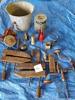 Photo of vintage tools arranged on blue tarp including metal bucket, carpenters clamps, oil cans, sharpening stone, hand drills, and miscellaneous hand tools.