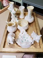 Photo of Belleek porcelain vases, creamer, sugar bowl and animal figurines on wooden tray.