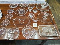 Wide view of assorted Candlewick crystal platters, divided trays, small bowls, candle holders arranged on wooden table.