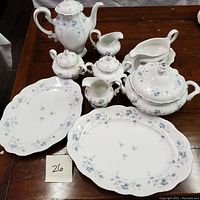 Full set of Johann Havilland Bavarian china on wooden table showcasing teapot, sugar bowls, creamer, tureen, gravy boat, and two large oval platters, all decorated with blue floral patterns and silver trim.